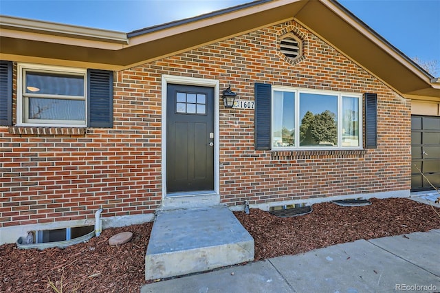 view of exterior entry with crawl space, a garage, and brick siding