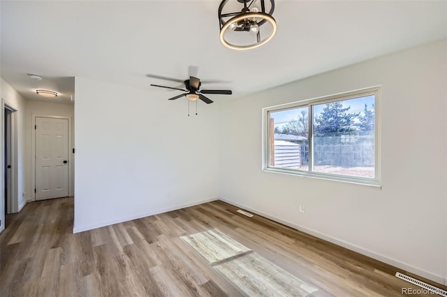 empty room with a ceiling fan, visible vents, baseboards, and wood finished floors