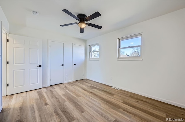 unfurnished bedroom featuring light wood finished floors, baseboards, visible vents, a ceiling fan, and multiple closets