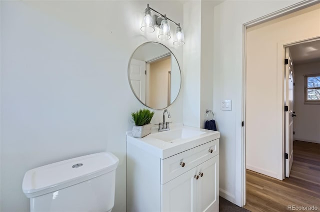 half bath featuring toilet, wood finished floors, vanity, and baseboards