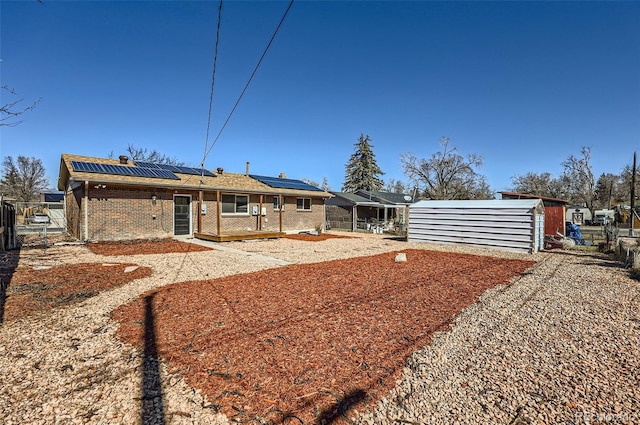 back of house with brick siding, fence, and roof mounted solar panels