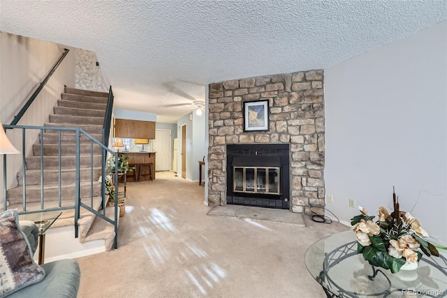 carpeted living room featuring stairway, a textured ceiling, a stone fireplace, and ceiling fan