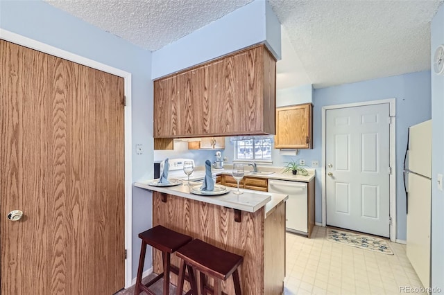 kitchen featuring white appliances, a textured ceiling, light countertops, a kitchen breakfast bar, and a sink