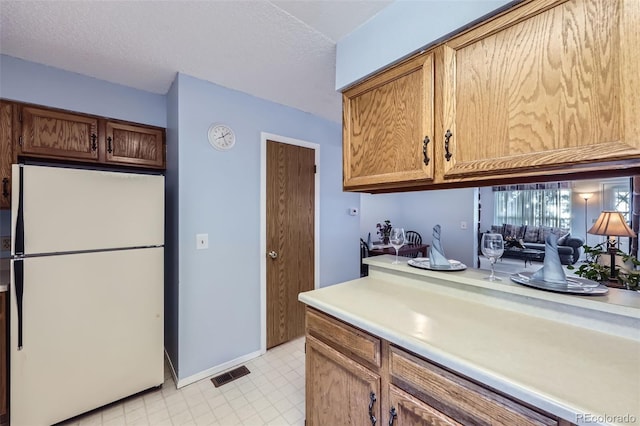 kitchen featuring freestanding refrigerator, light countertops, light flooring, a textured ceiling, and baseboards