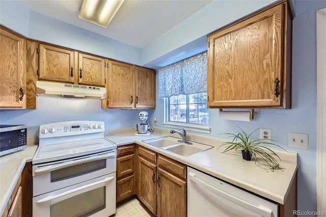 kitchen featuring under cabinet range hood, white appliances, a sink, and light countertops