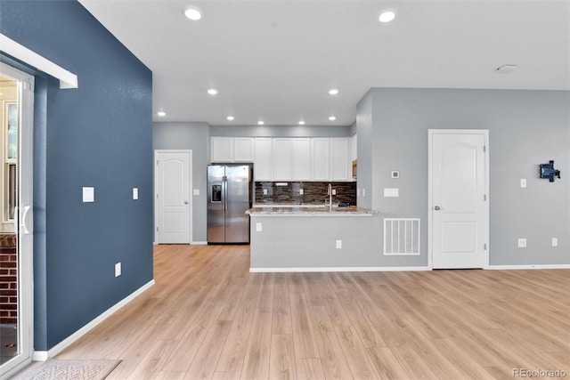 kitchen with white cabinetry, light stone countertops, stainless steel fridge with ice dispenser, backsplash, and kitchen peninsula