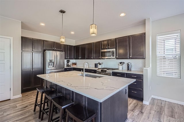 kitchen featuring hanging light fixtures, sink, light wood-type flooring, an island with sink, and stainless steel appliances