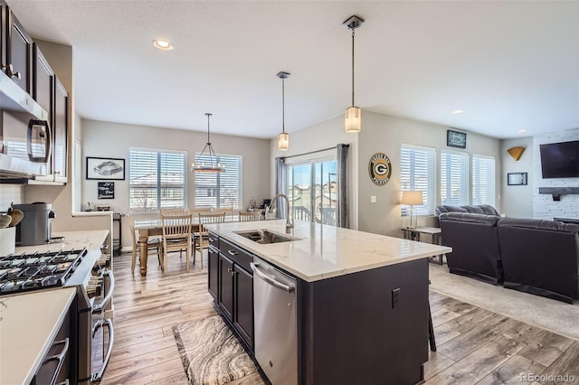 kitchen featuring light stone countertops, a kitchen island with sink, sink, pendant lighting, and stainless steel appliances