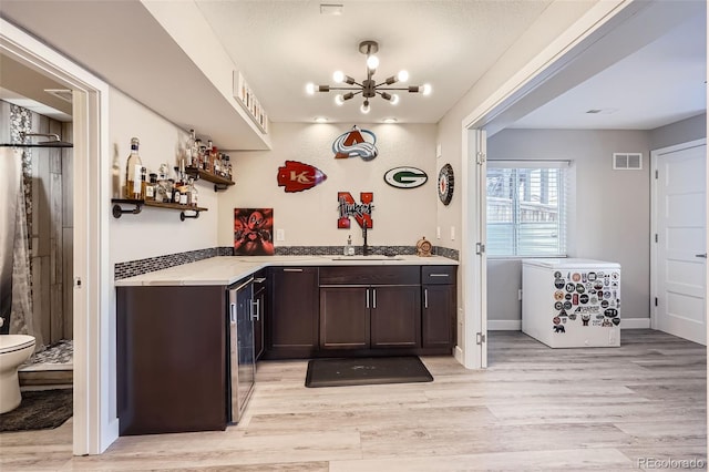 bar with sink, light hardwood / wood-style floors, a chandelier, and dark brown cabinetry