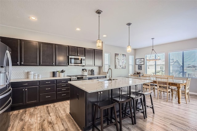 kitchen with decorative light fixtures, stainless steel appliances, tasteful backsplash, an island with sink, and sink