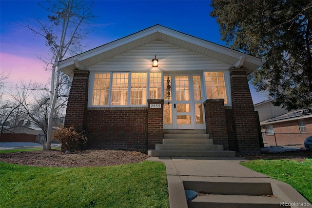 bungalow-style home featuring entry steps, brick siding, and a lawn