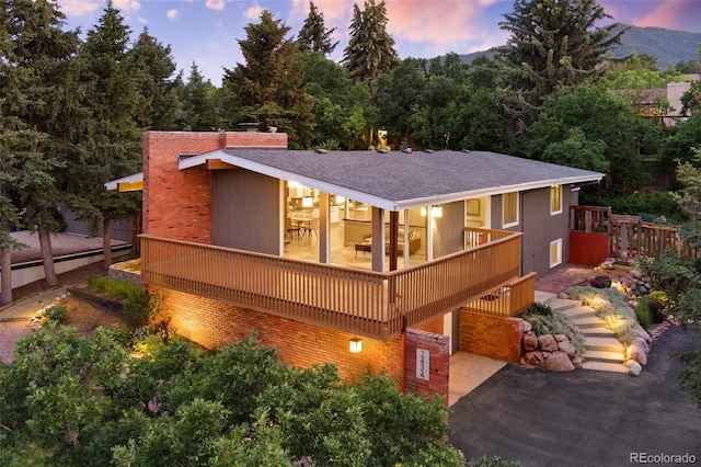 2434 Virgo Dr, Colorado Springs, CO 80906 - back of house at dusk featuring a shingled roof, asphalt driveway, an attached garage, a chimney, and stairway
