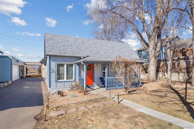 bungalow-style house featuring a porch, an outdoor structure, fence, roof with shingles, and board and batten siding