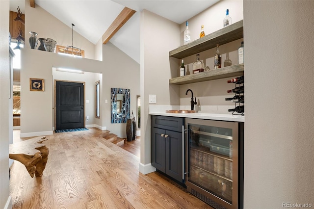 bar with beverage cooler, high vaulted ceiling, wet bar, a sink, and light wood-type flooring