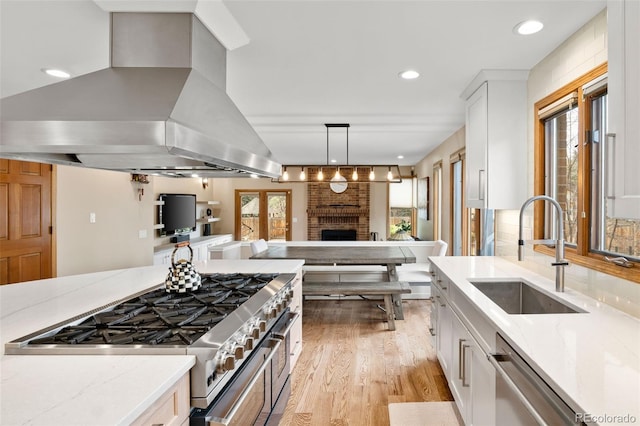 kitchen featuring a sink, island exhaust hood, stove, white cabinetry, and stainless steel dishwasher