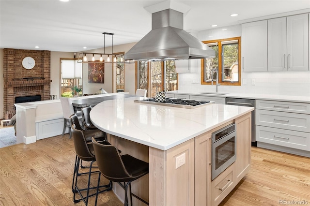 kitchen with light wood-type flooring, island exhaust hood, a sink, a kitchen breakfast bar, and stainless steel appliances