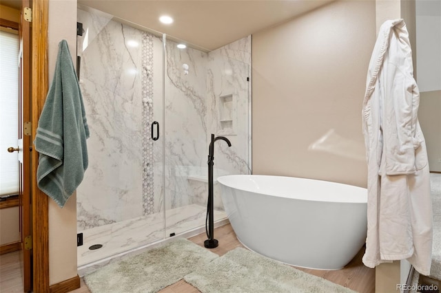 bathroom featuring recessed lighting, a marble finish shower, a freestanding bath, and wood finished floors