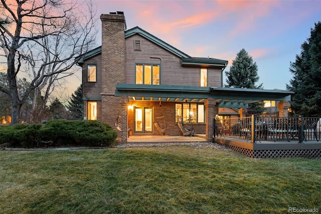 back of house at dusk with a yard, brick siding, and a chimney