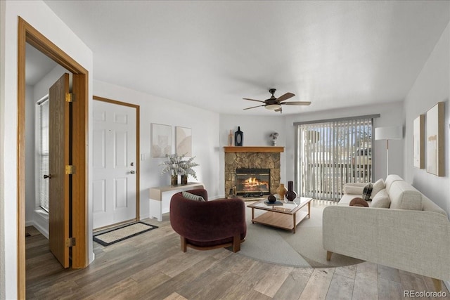 living room with hardwood / wood-style flooring, ceiling fan, and a stone fireplace