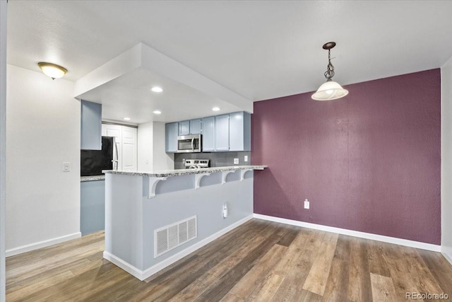 kitchen featuring hardwood / wood-style flooring, appliances with stainless steel finishes, white cabinetry, hanging light fixtures, and kitchen peninsula