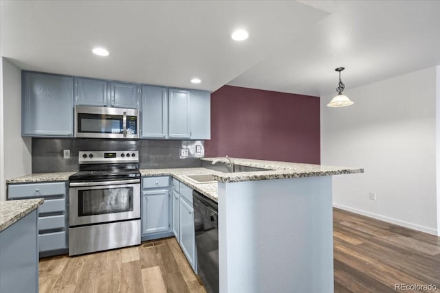 kitchen featuring stainless steel appliances, decorative light fixtures, kitchen peninsula, and hardwood / wood-style floors