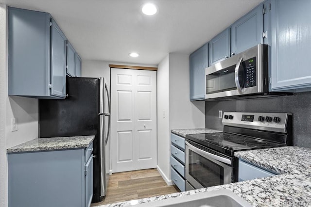 kitchen featuring blue cabinets, light stone countertops, light hardwood / wood-style floors, and appliances with stainless steel finishes