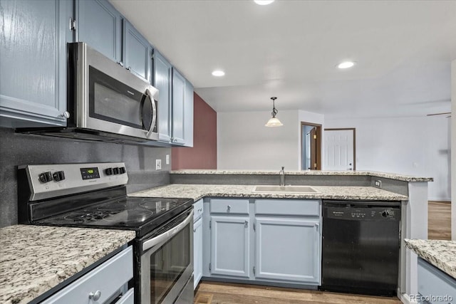 kitchen featuring appliances with stainless steel finishes, wood-type flooring, sink, hanging light fixtures, and kitchen peninsula