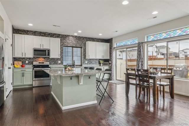 kitchen featuring a breakfast bar area, light stone countertops, appliances with stainless steel finishes, visible vents, and dark wood-style flooring