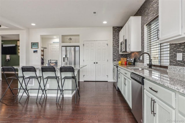 kitchen featuring a sink, a breakfast bar area, stainless steel appliances, white cabinets, and dark wood-type flooring