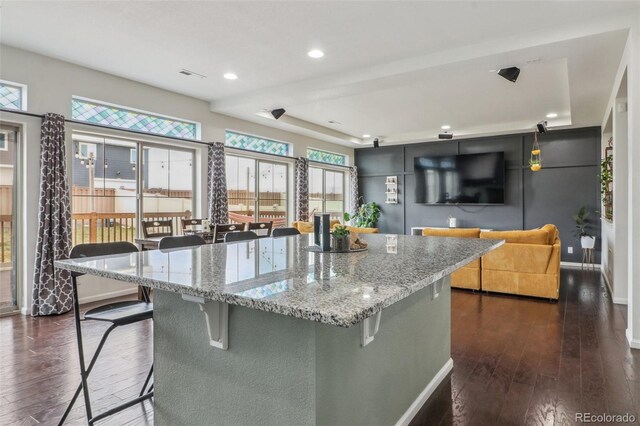 kitchen featuring dark wood-type flooring, a kitchen bar, light stone countertops, and visible vents