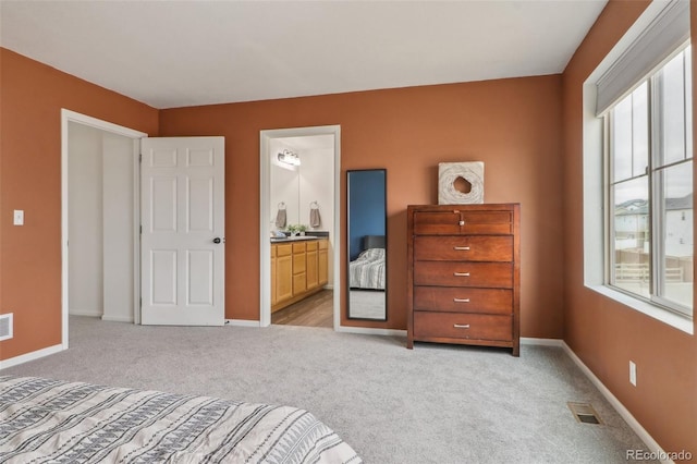 bedroom featuring ensuite bathroom, baseboards, light colored carpet, and visible vents