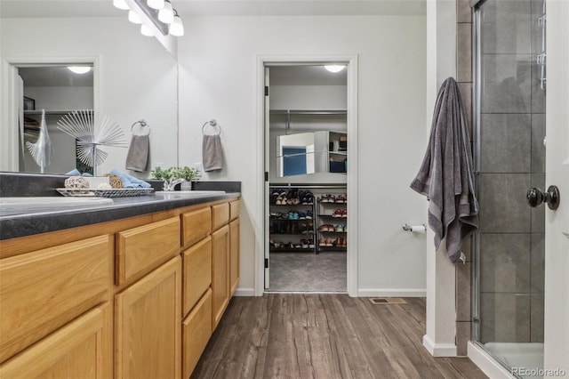 full bathroom with a spacious closet, wood finished floors, vanity, and a shower stall