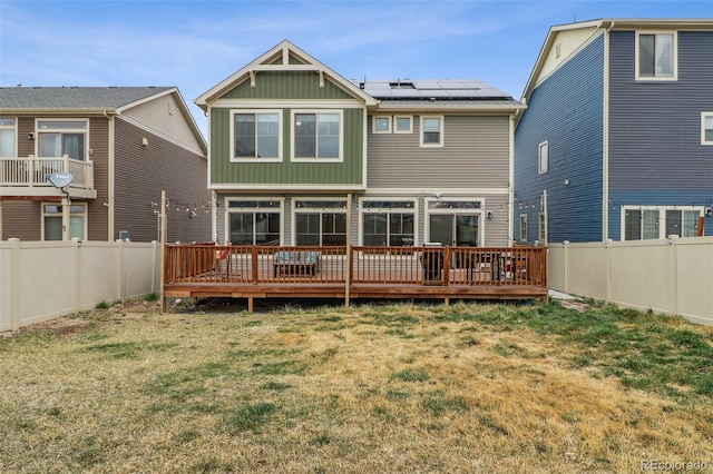 rear view of house with a fenced backyard, roof mounted solar panels, a deck, and a lawn