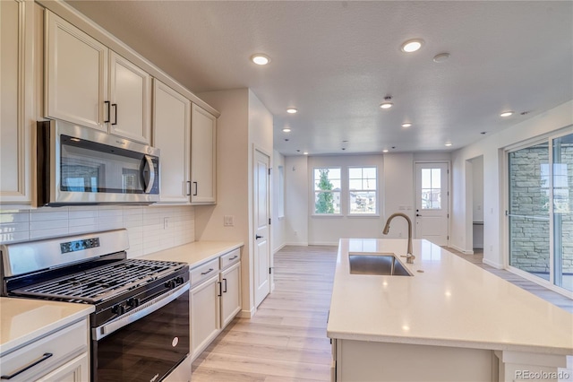 kitchen featuring light wood finished floors, a sink, stainless steel appliances, light countertops, and backsplash