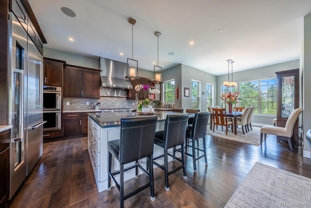 230 S Big Meadow Trl, Franktown, CO 80116 - kitchen featuring wall chimney range hood, stainless steel appliances, dark brown cabinets, dark wood finished floors, and recessed lighting