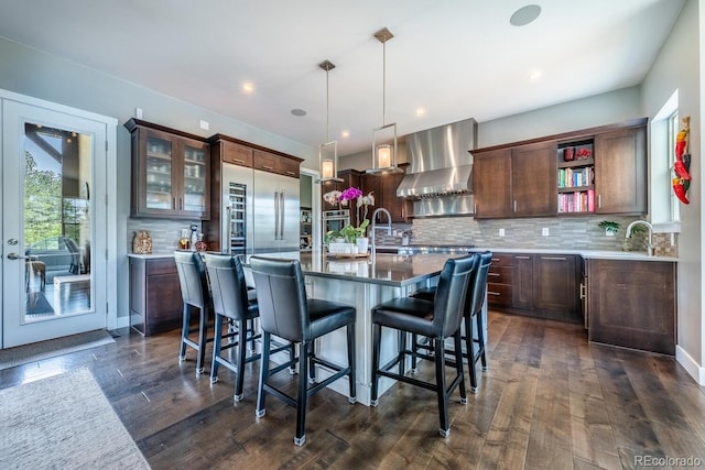 230 S Big Meadow Trl, Franktown, CO 80116 - kitchen featuring wall chimney range hood, tasteful backsplash, open shelves, an island with sink, and a kitchen breakfast bar