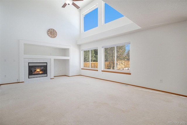 unfurnished living room featuring a tile fireplace, light carpet, a towering ceiling, and ceiling fan