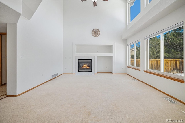 unfurnished living room with carpet flooring, a tiled fireplace, ceiling fan, and a high ceiling