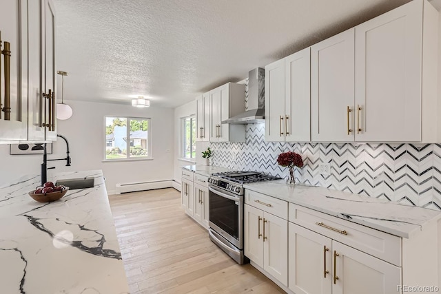 kitchen with decorative light fixtures, stainless steel gas range, baseboard heating, wall chimney range hood, and light stone countertops