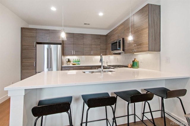 kitchen featuring sink, kitchen peninsula, a kitchen bar, appliances with stainless steel finishes, and hardwood / wood-style flooring