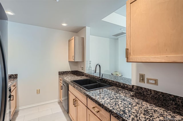 kitchen featuring stainless steel dishwasher, light brown cabinets, dark stone countertops, and sink