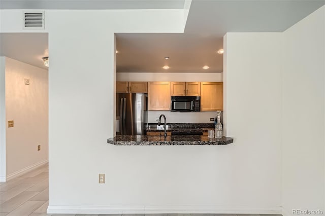 kitchen with kitchen peninsula, stainless steel refrigerator, light brown cabinets, and dark stone counters