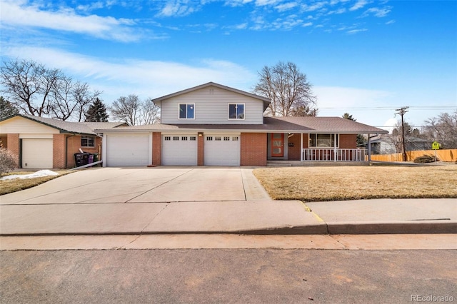 split level home featuring a garage, concrete driveway, a porch, a front lawn, and brick siding