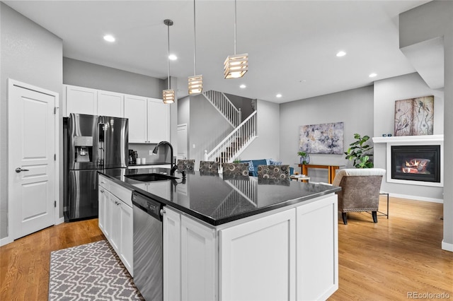 kitchen with appliances with stainless steel finishes, a center island with sink, white cabinetry, and a sink
