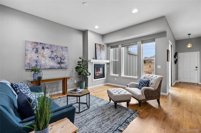 living area with recessed lighting, a glass covered fireplace, wood finished floors, and baseboards