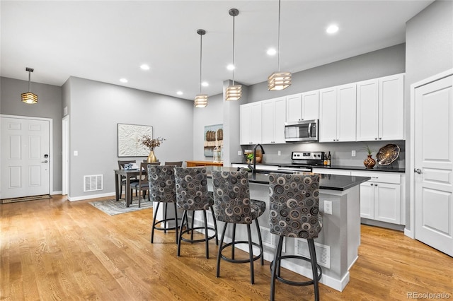kitchen featuring an island with sink, stainless steel appliances, dark countertops, visible vents, and a kitchen bar