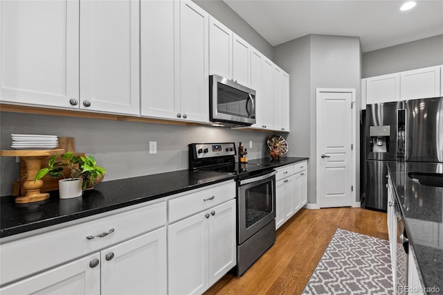 kitchen featuring dark stone counters, white cabinets, stainless steel appliances, and light wood-type flooring