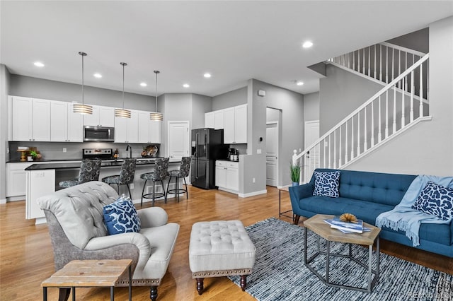 living room featuring recessed lighting, light wood-style flooring, baseboards, and stairway