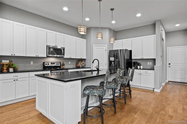 kitchen with dark countertops, hanging light fixtures, a sink, stainless steel appliances, and a center island with sink