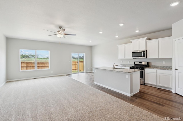 kitchen featuring appliances with stainless steel finishes, light stone counters, a kitchen island with sink, sink, and white cabinets